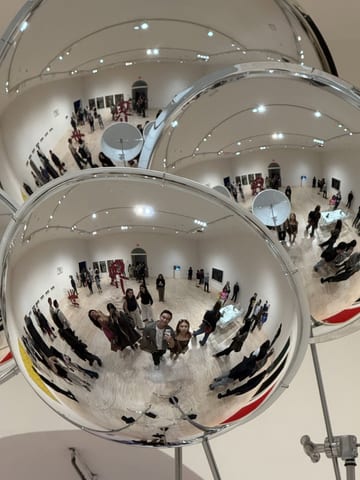 Visitors reflected in a mirrored spherical artwork at MoMA PS1