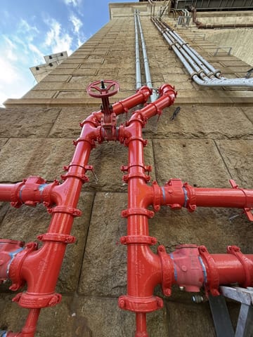 Bright red pipes rising along the base of the Queensboro Bridge