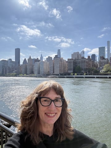 Stacy smiling with the Manhattan skyline across the East River behind her