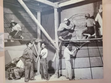 Historic black-and-white photograph of artists working on the mural from scaffolding